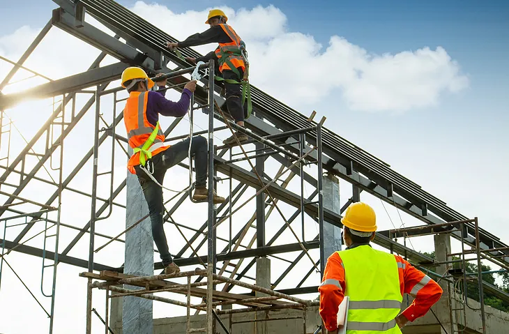 Workers in safety gear climbing a steel roof structure